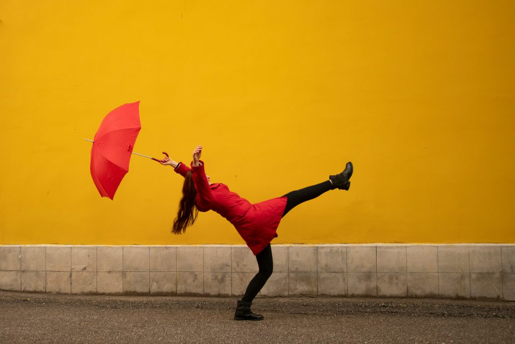 zdjęcie dziewczyny w czerwonych ubraniach trzymająca czerwoną parasolkę na żółtym tle