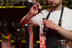 Mężczyzna w ciemnym pomieszczeniu robi drinki za pomocą shakera - kursy barmańskie