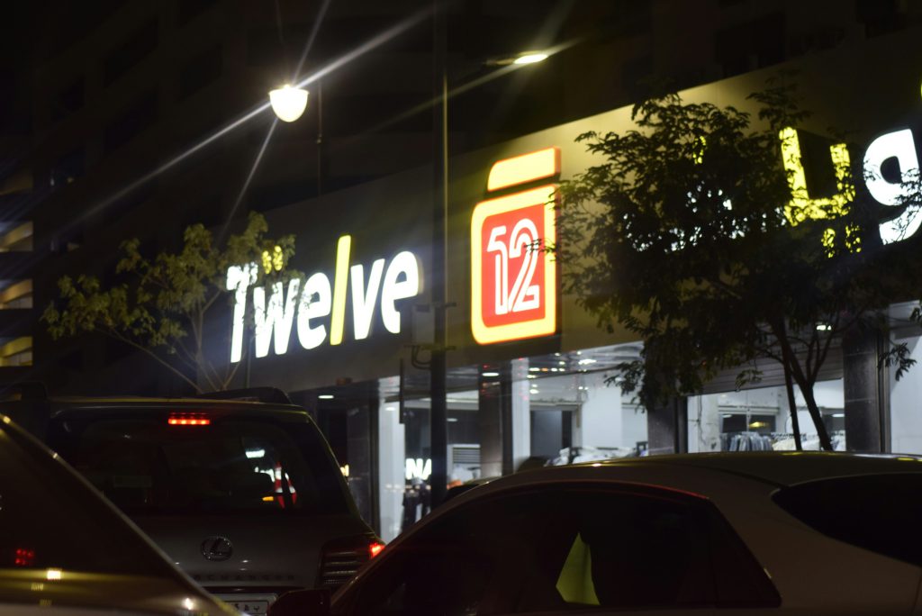 Na zdjęciu widać nocną ulicę w mieście, oświetloną światłem latarni i neonowych szyldów sklepowych